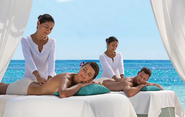 Couples enjoying beachfront massages under a shaded cabana at Secrets Akumal Riviera Maya with turquoise Caribbean views.